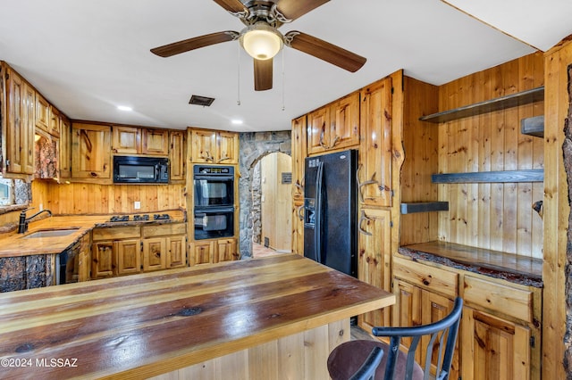 kitchen with kitchen peninsula, sink, wood walls, and black appliances