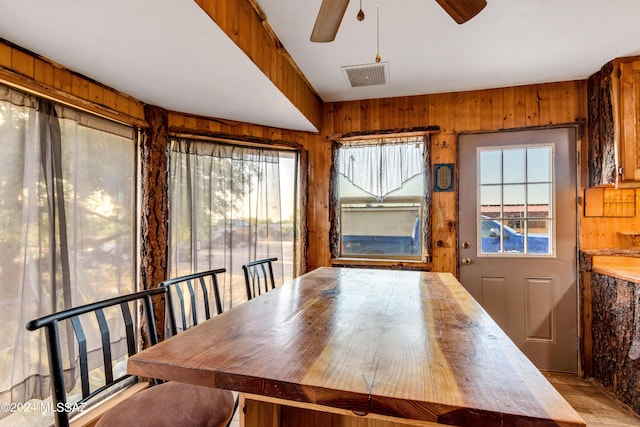 unfurnished dining area featuring wooden walls, ceiling fan, and a healthy amount of sunlight