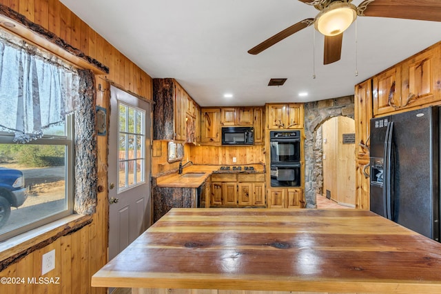 kitchen featuring wood walls, sink, butcher block counters, and black appliances