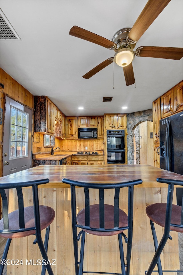 kitchen with kitchen peninsula, ceiling fan, wooden walls, and black appliances