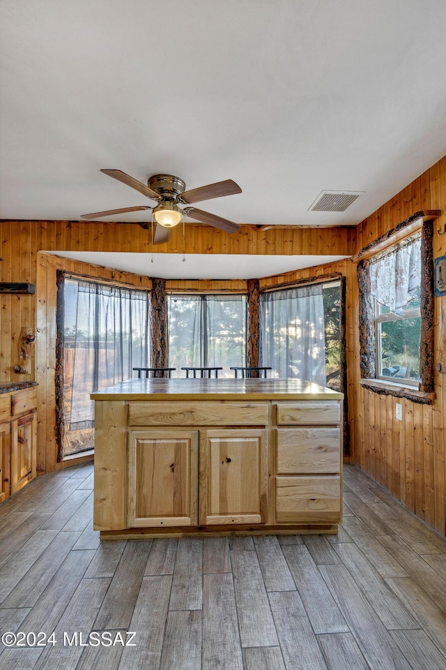 kitchen with ceiling fan, light brown cabinets, light wood-type flooring, and wooden walls