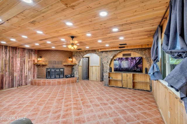 unfurnished living room with ceiling fan, a fireplace, wood ceiling, and wood walls