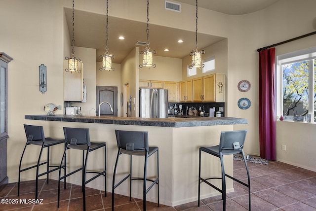 kitchen featuring kitchen peninsula, light brown cabinetry, tasteful backsplash, a breakfast bar, and stainless steel refrigerator