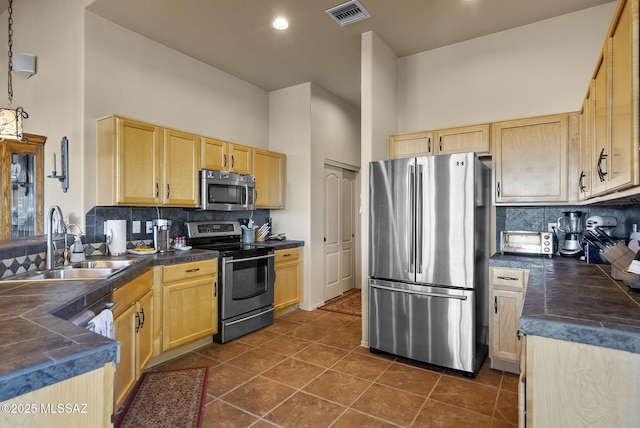 kitchen featuring sink, light brown cabinets, a towering ceiling, dark tile patterned flooring, and appliances with stainless steel finishes