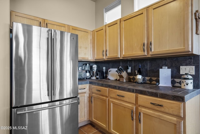 kitchen featuring tile patterned flooring, decorative backsplash, light brown cabinetry, and stainless steel refrigerator