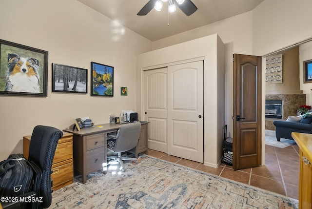 tiled office space with ceiling fan and a fireplace