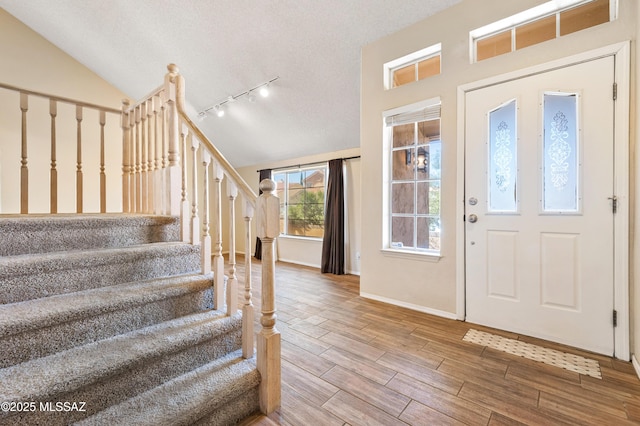 foyer entrance featuring rail lighting, lofted ceiling, and a textured ceiling