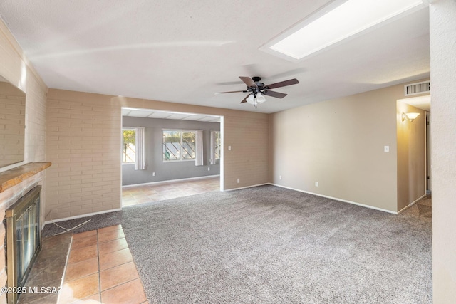 unfurnished living room with ceiling fan, a large fireplace, brick wall, and carpet