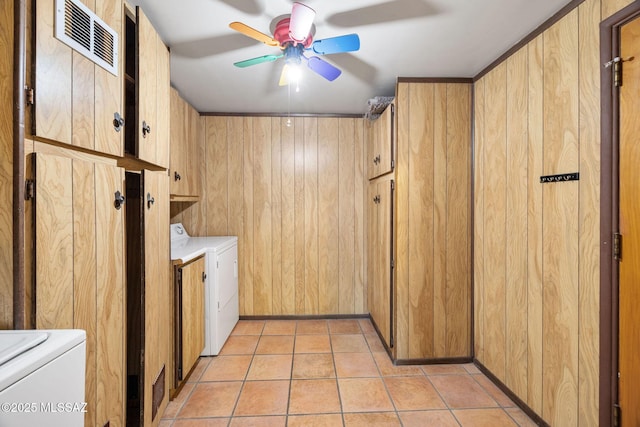 clothes washing area with light tile patterned flooring, cabinets, wooden walls, and washer and dryer