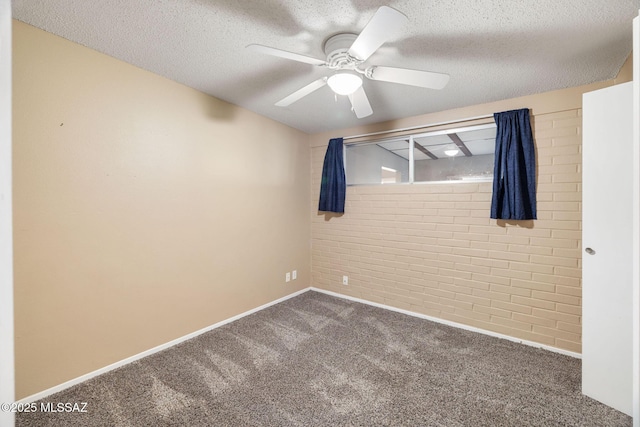 empty room with ceiling fan, brick wall, dark carpet, and a textured ceiling