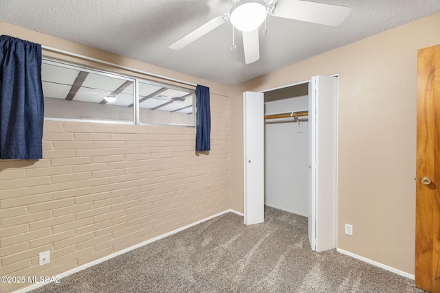 unfurnished bedroom with ceiling fan, carpet floors, a textured ceiling, brick wall, and a closet