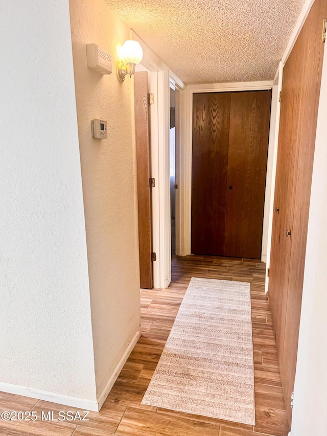 hall featuring a textured wall, a textured ceiling, baseboards, and wood finished floors