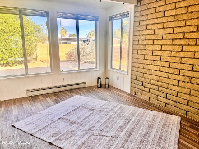 empty room featuring plenty of natural light, a baseboard radiator, brick wall, and wood finished floors