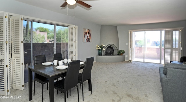 dining space with a large fireplace, ceiling fan, and carpet