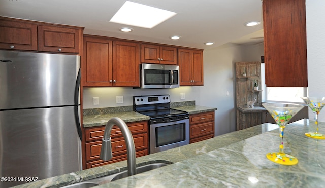 kitchen featuring light stone counters, appliances with stainless steel finishes, a skylight, and sink