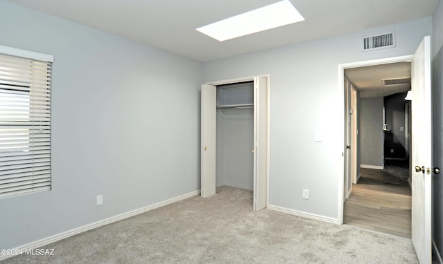 unfurnished bedroom with a skylight, a closet, and light carpet