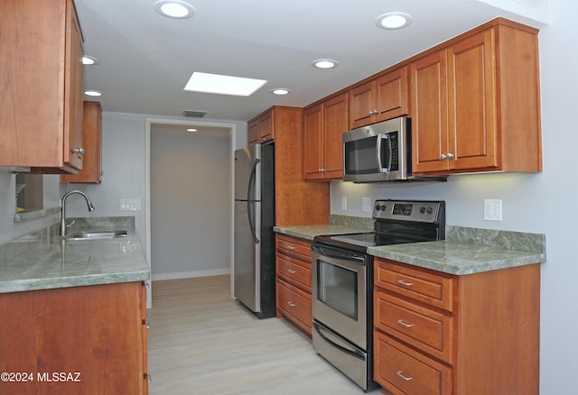 kitchen featuring appliances with stainless steel finishes, light hardwood / wood-style flooring, a skylight, and sink