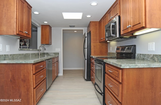 kitchen with stainless steel appliances, a skylight, light stone countertops, sink, and light hardwood / wood-style flooring