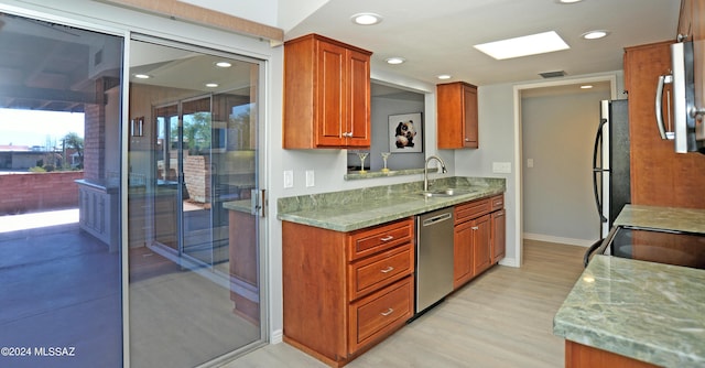 kitchen with stainless steel appliances, sink, light wood-type flooring, and light stone countertops