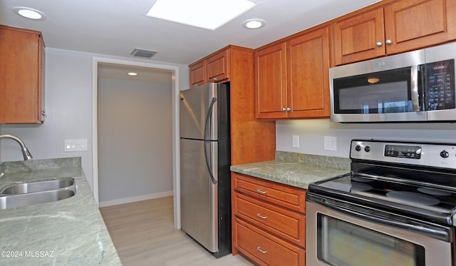 kitchen featuring stainless steel appliances, light wood-type flooring, a skylight, light stone counters, and sink