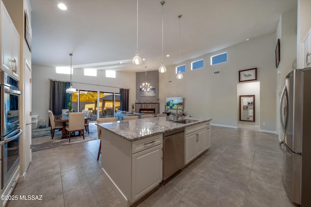 kitchen with appliances with stainless steel finishes, a center island with sink, white cabinetry, and hanging light fixtures