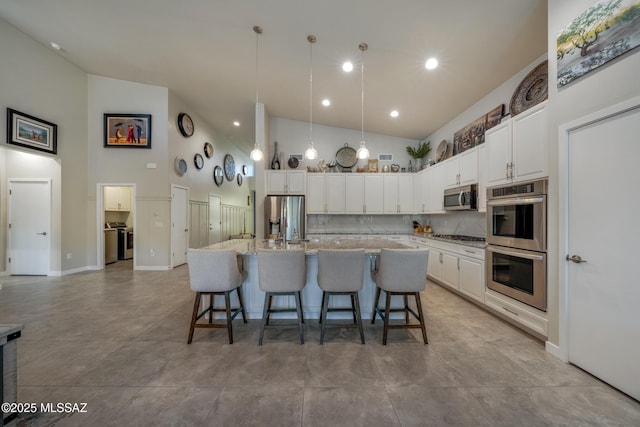 kitchen featuring a kitchen breakfast bar, light stone counters, an island with sink, white cabinets, and appliances with stainless steel finishes