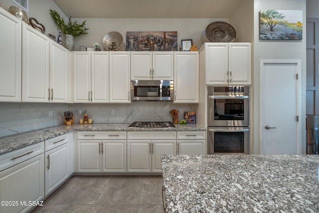 kitchen with white cabinets, light tile patterned floors, light stone countertops, appliances with stainless steel finishes, and tasteful backsplash