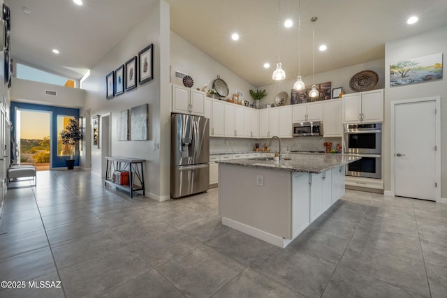 kitchen with white cabinets, light stone counters, stainless steel appliances, visible vents, and a sink