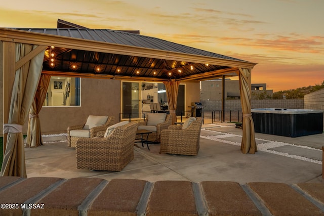 patio terrace at dusk with a gazebo, an outdoor living space, a hot tub, and grilling area