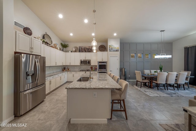 kitchen featuring a sink, recessed lighting, a kitchen bar, light stone counters, and appliances with stainless steel finishes