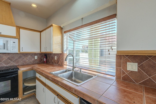 kitchen featuring tile counters, black range with electric stovetop, white microwave, white cabinets, and a sink