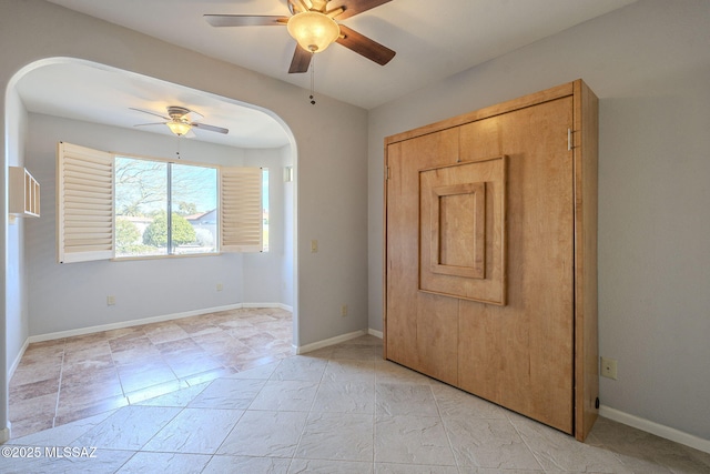 spare room with arched walkways, a ceiling fan, and baseboards