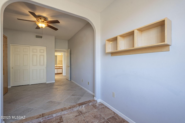 corridor with arched walkways, stone finish floor, visible vents, and baseboards