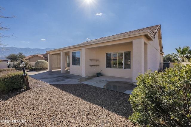 back of property with a patio, a mountain view, and stucco siding