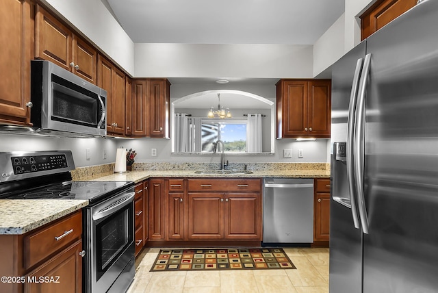 kitchen with light stone countertops, appliances with stainless steel finishes, a notable chandelier, and sink