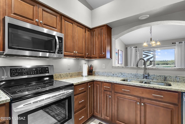 kitchen featuring light stone countertops, sink, appliances with stainless steel finishes, and an inviting chandelier