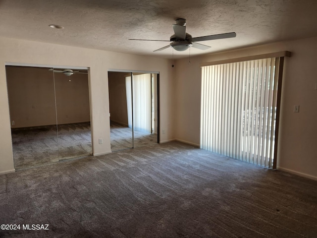 unfurnished bedroom featuring ceiling fan, carpet floors, a textured ceiling, and multiple closets