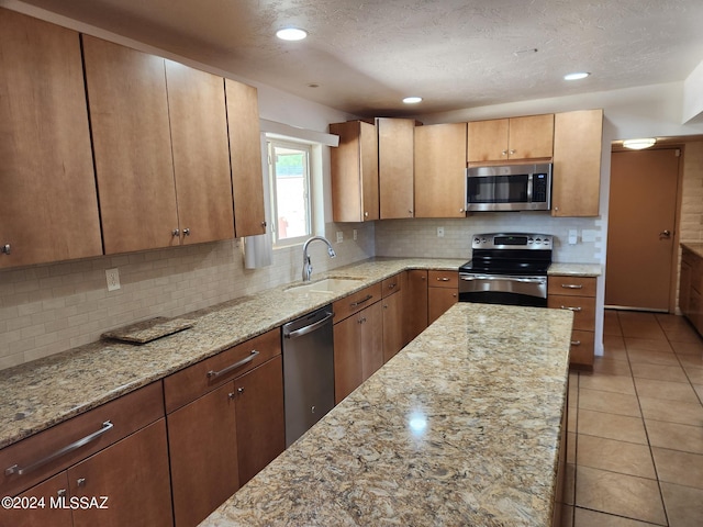 kitchen featuring light stone countertops, backsplash, stainless steel appliances, and sink