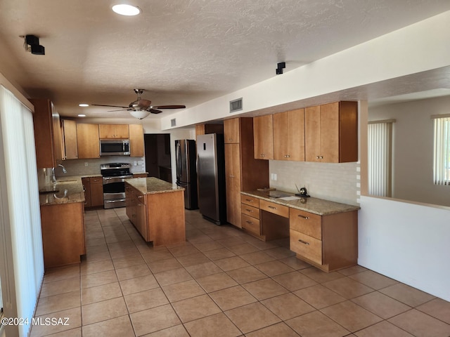 kitchen featuring a center island, sink, ceiling fan, light tile patterned flooring, and stainless steel appliances