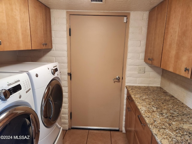 clothes washing area with washer and dryer, cabinets, and light tile patterned floors