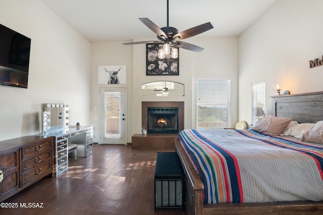 bedroom featuring dark wood-style floors, access to exterior, a lit fireplace, and a high ceiling