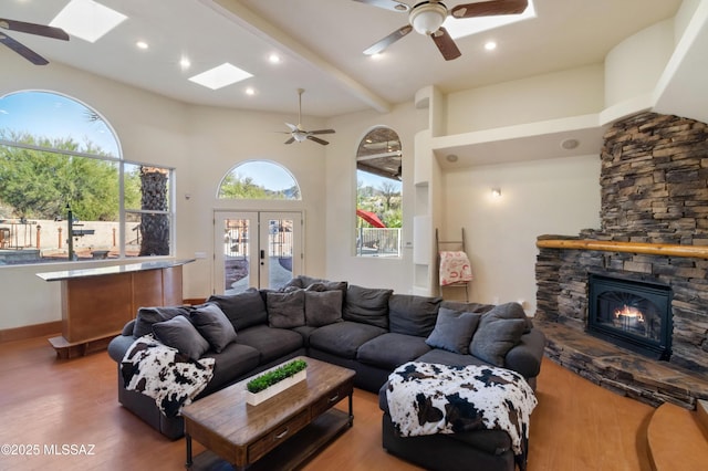 living area with a skylight, beam ceiling, french doors, a stone fireplace, and wood finished floors