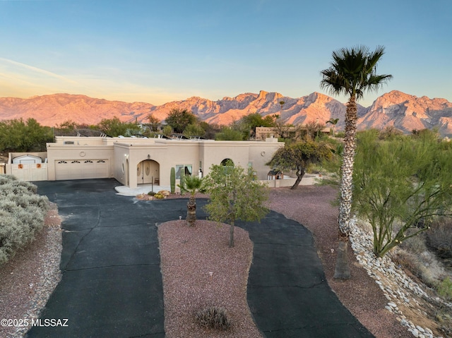 adobe home featuring driveway, an attached garage, fence, a mountain view, and stucco siding