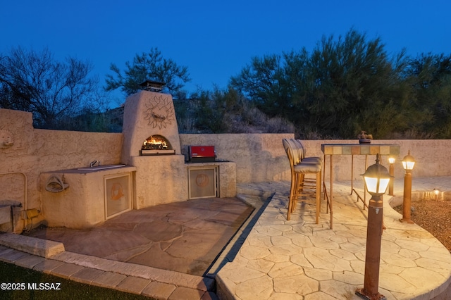 view of patio with a warm lit fireplace, area for grilling, and exterior bar