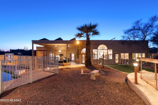 back of house at dusk featuring a patio and stucco siding