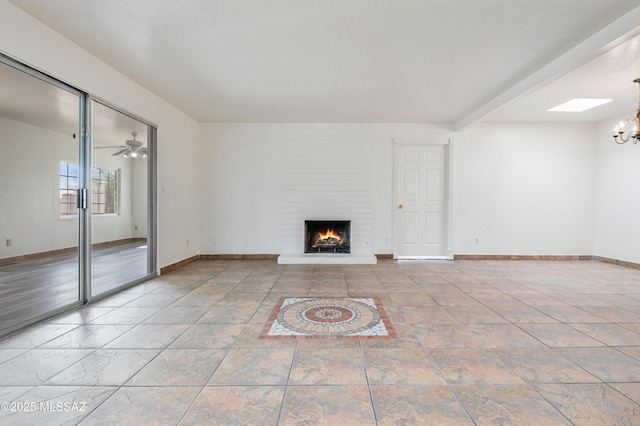 unfurnished living room featuring a skylight, ceiling fan with notable chandelier, and a fireplace