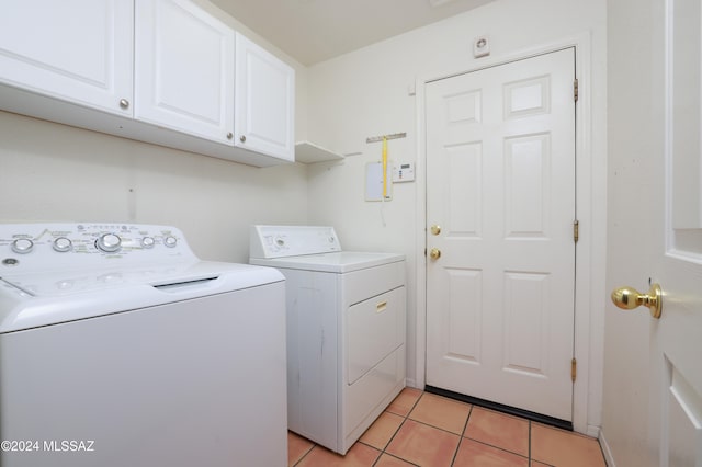 laundry room with washing machine and clothes dryer, light tile patterned floors, and cabinets