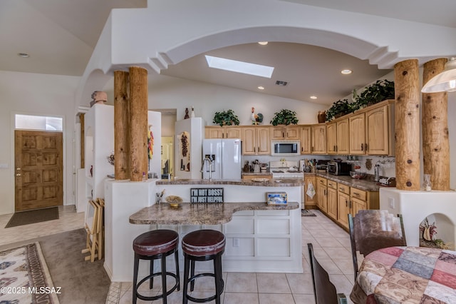 kitchen featuring lofted ceiling with skylight, a kitchen bar, fridge with ice dispenser, light tile patterned flooring, and white gas stove