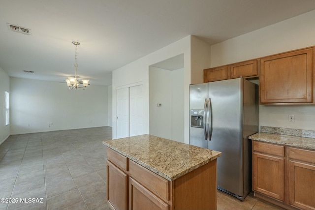 kitchen with stainless steel refrigerator with ice dispenser, a center island, a chandelier, and light stone counters