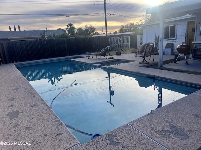 pool at dusk with a grill and a patio area